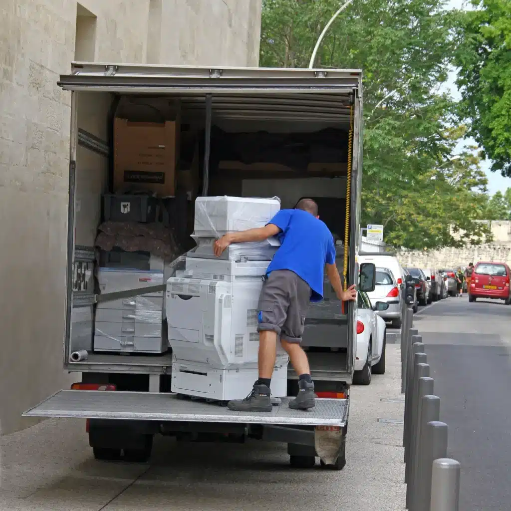 Un déménageur charge une photocopieuse dans un camion lors du transfert d’une association ou d’un organisme, illustrant un déménagement professionnel organisé et sécurisé. ​​