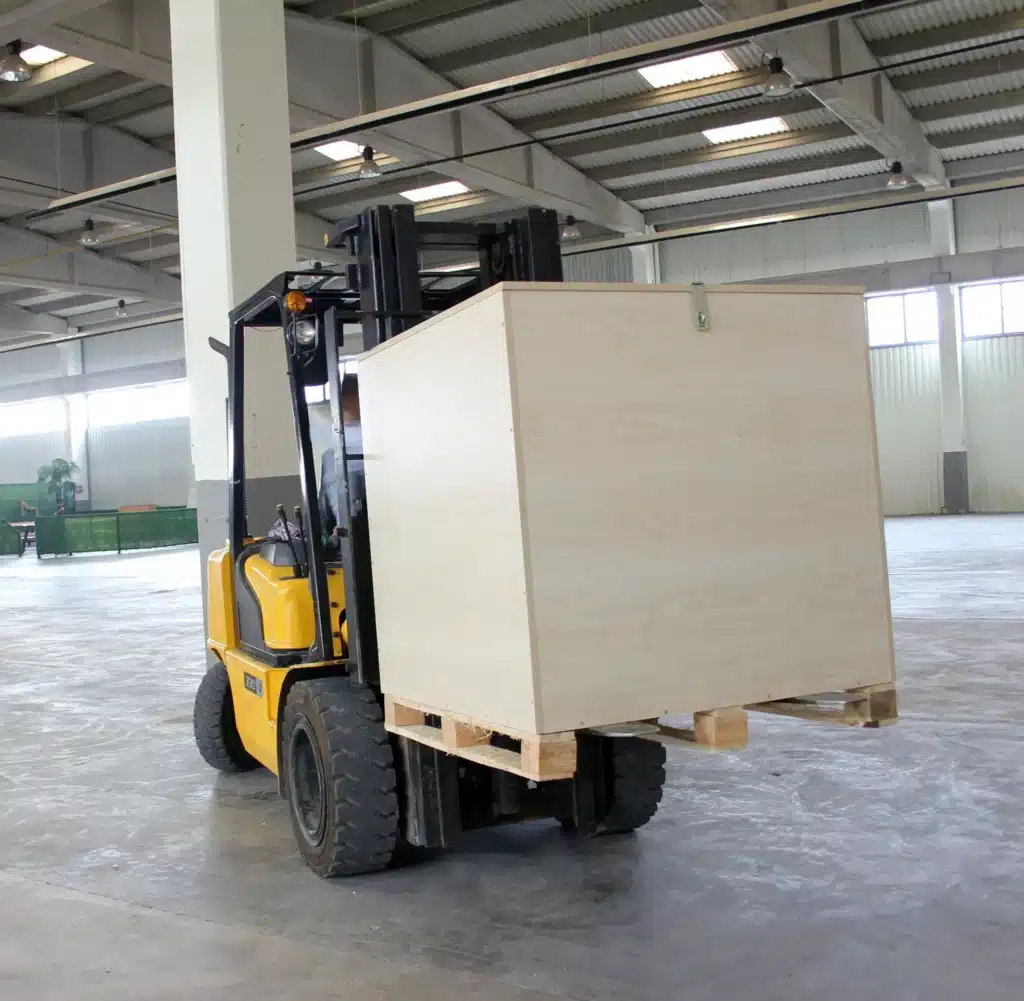 Un chariot élévateur transportant une grande caisse en bois, illustrant le déménagement professionnel de matériel volumineux.